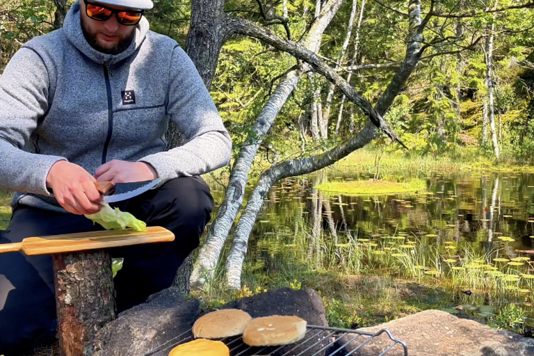 Man som förbereder mat vid en sjö, med pannkakor som grillas på en öppen eld.