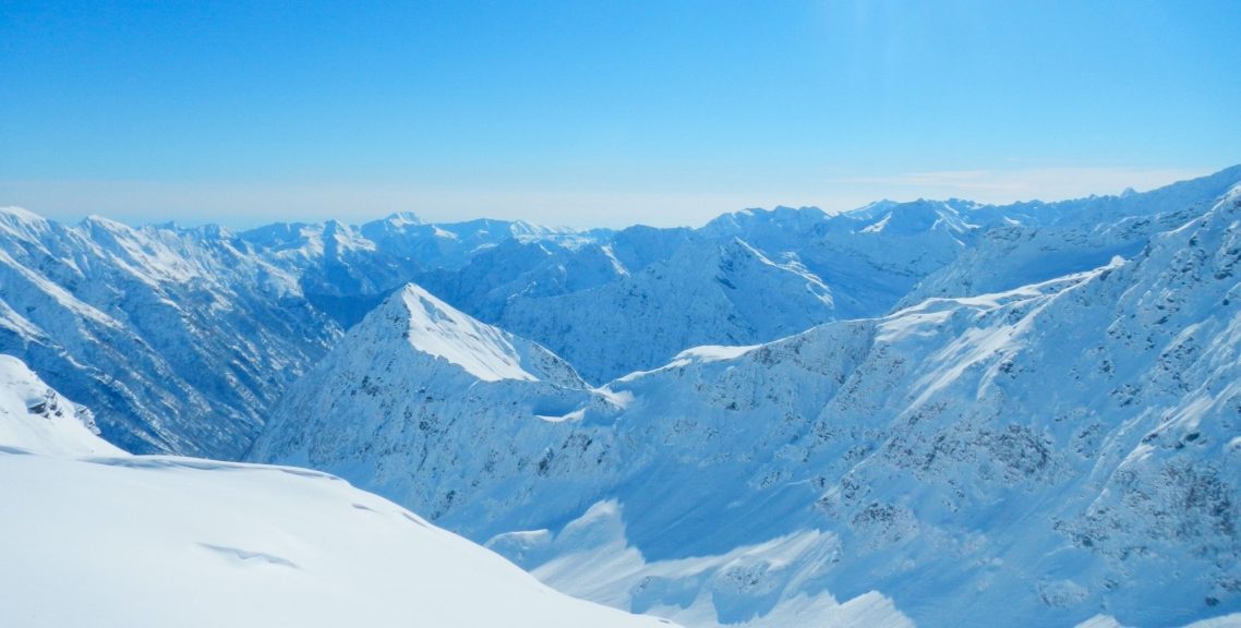 Snöklädda berg med klarblå himmel och fjärran dalar.