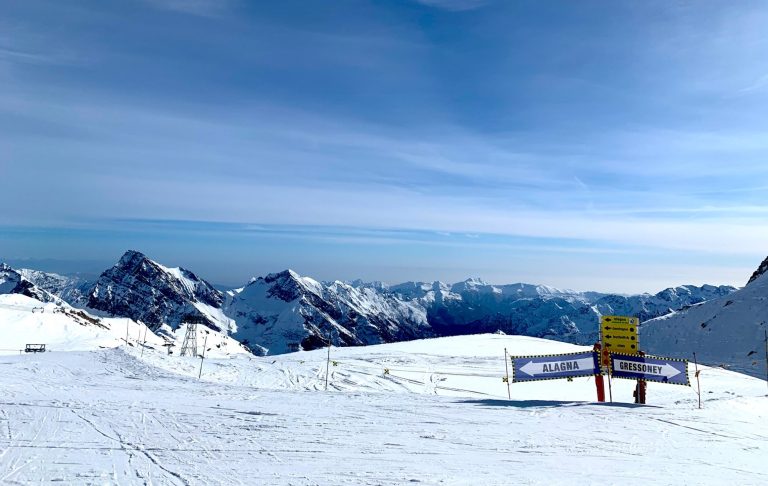 Snötäckta bergstoppar under en klar, blå himmel. En gul skylt i förgrunden.