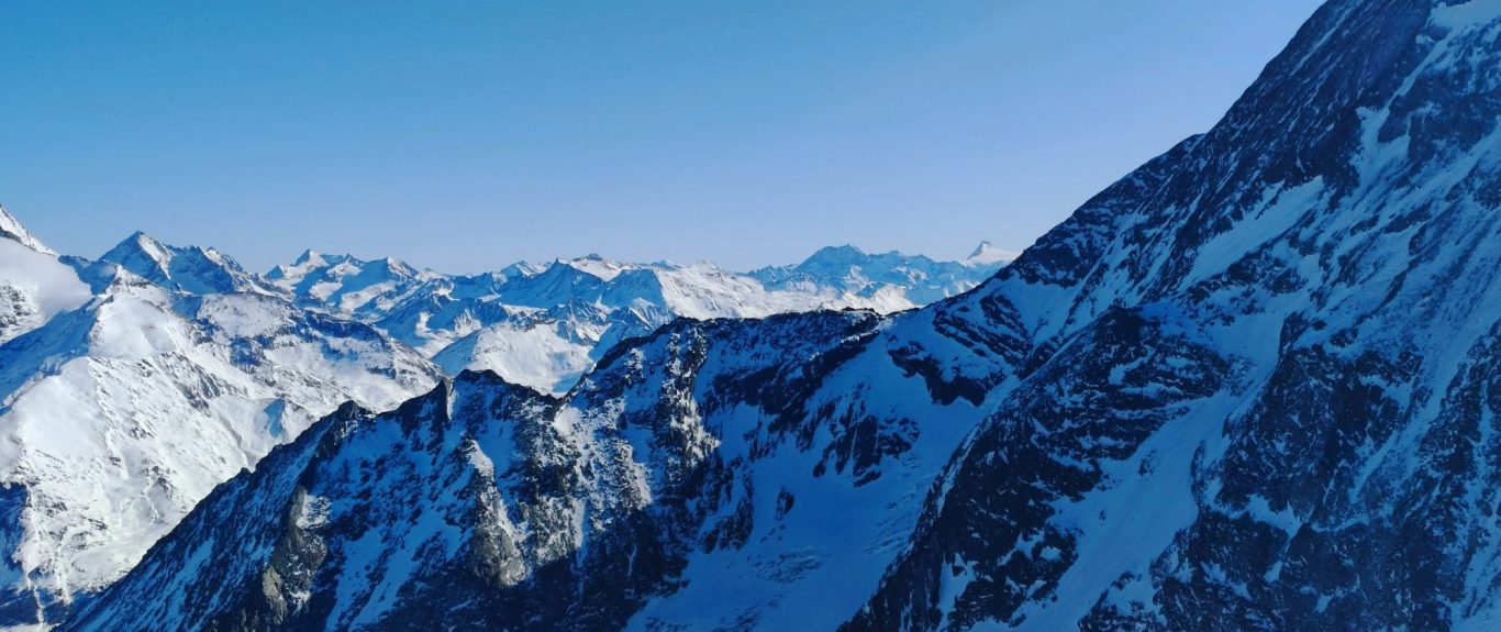 Snötäckta alpberg och fjäll under en klarblå himmel.