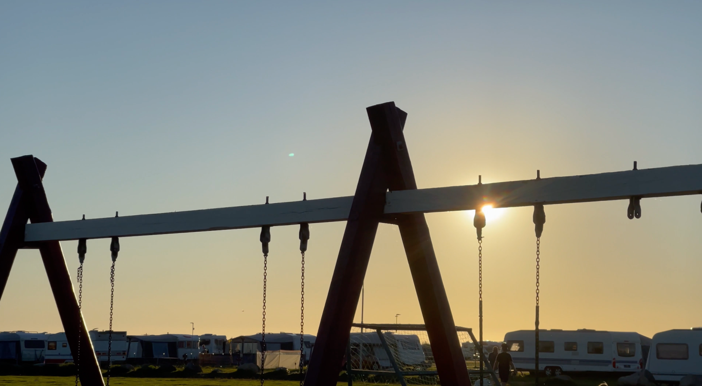 Solnedgång över Campingen i Björkäng Gungställning med solnedgång i bakgrunden, campingvagnar syns i fjärran.