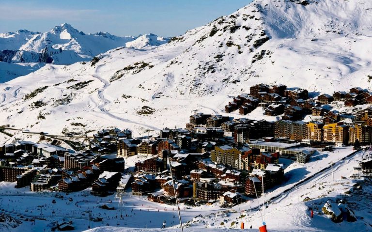 Fjällby med snötäckta hus och omgivande berg. Klart blå himmel i bakgrunden.