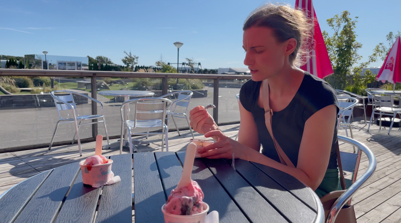 Äter glass Kvinna sitter vid ett bord och äter glass i soligt utomhusområde.