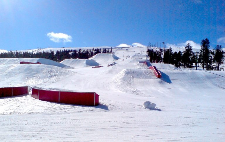 Snötäckta backar med ramp och hinder för skidåkning i soligt väder. Skipark