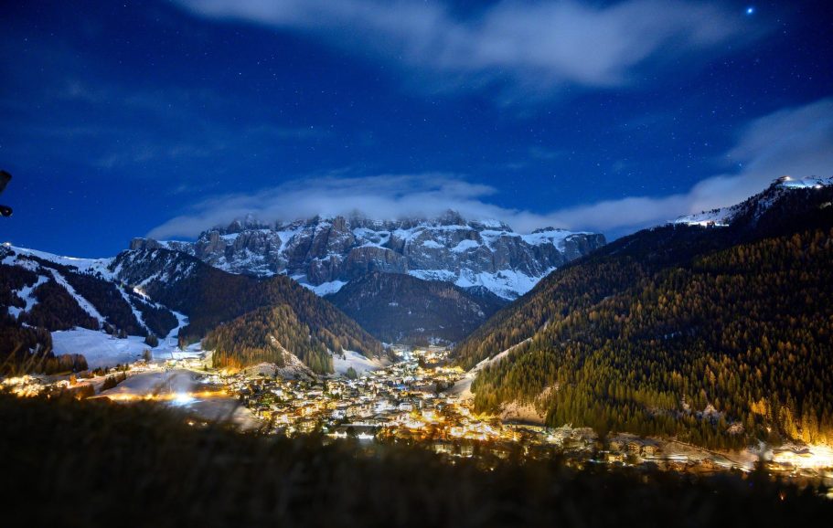 Val Gardena - Italien Nattvy över en snöklädd by omgiven av berg, upplyst av stjärnljus.