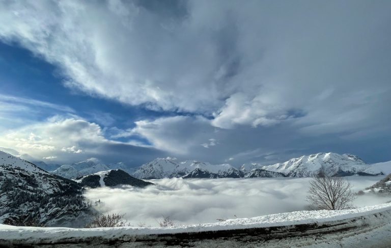 Snöklädda alpberg med moln och dimma som sträcker sig över dalen.