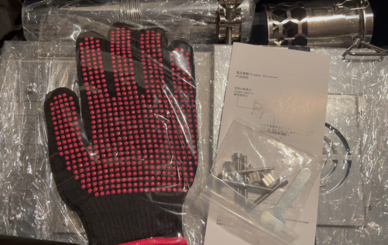 Svart handske med röda prickar, en plastpackad komponent och ett dokument.
