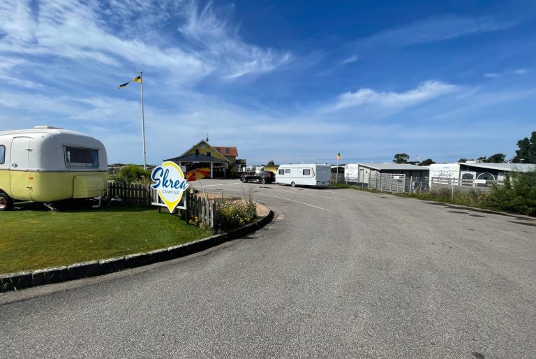 Skrea Campings Infart till Receptionen En grusväg som leder genom en campingplats med husvagnar och soligt väder.