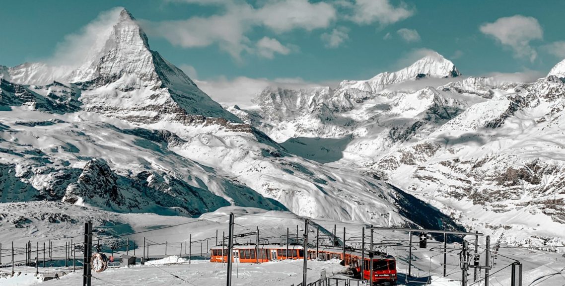 Rött alptåg åker genom snötäckta alpberg med den majestätiska matterhorn toppen i bakgrunden.