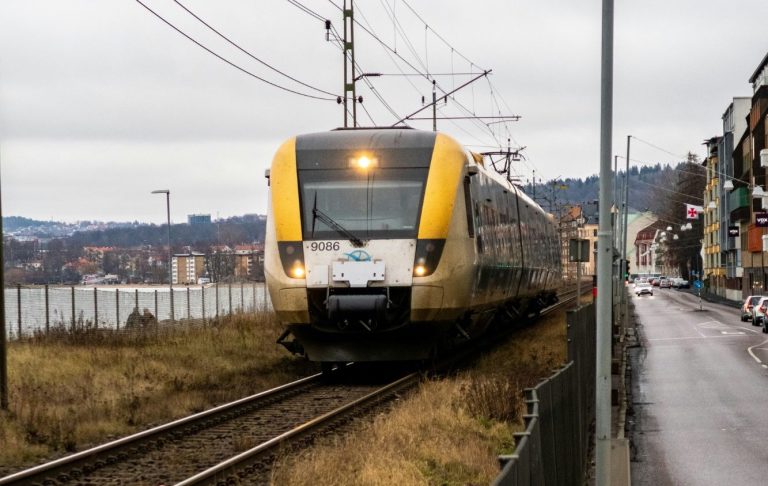 Koltåg närmar sig längs en spårvidd nära en väg och vattnet. Wetter grå himmel.