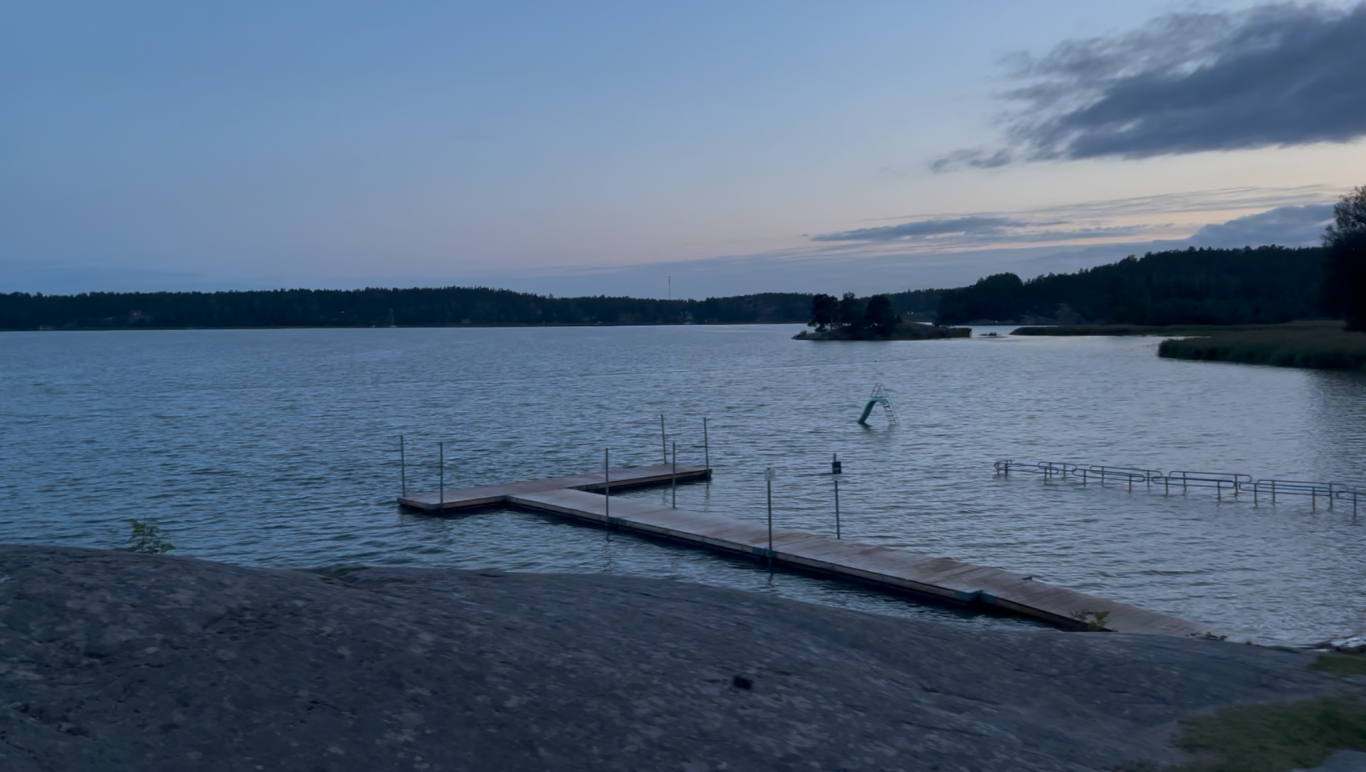 Badstranden och badbryggan En stilla sjö vid skymning med en brygga som sträcker sig ut i vattnet.