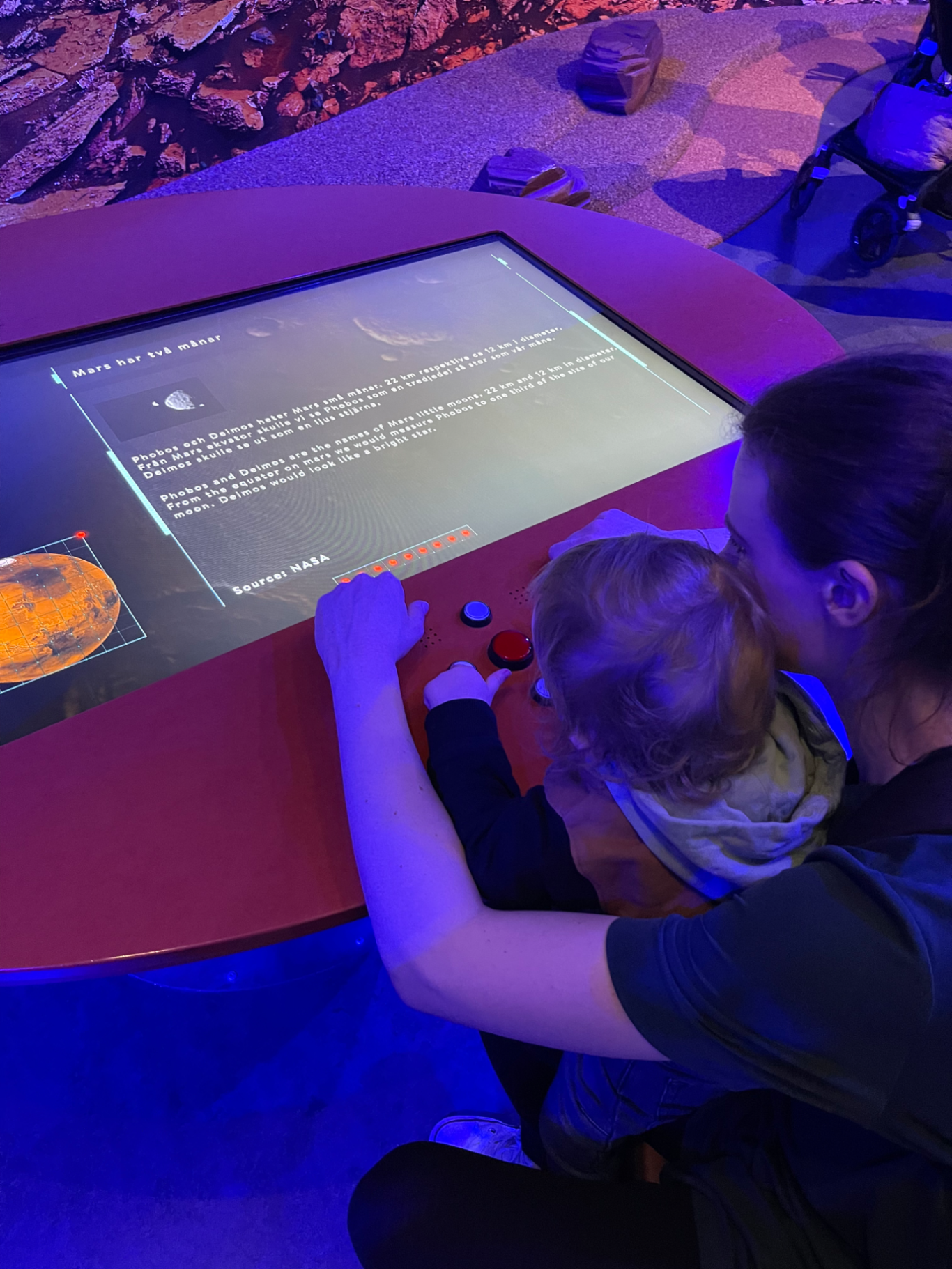 Universum En vuxen och ett barn interagerar med en pekskärm på en utställning.