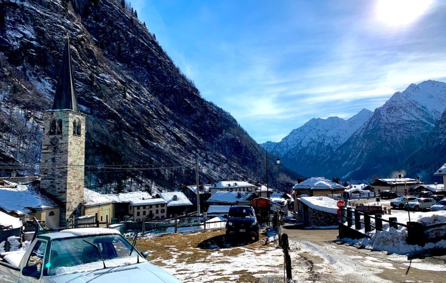 Vinterlandskap med snötäckta berg och en by med en kyrktorn i förgrunden.