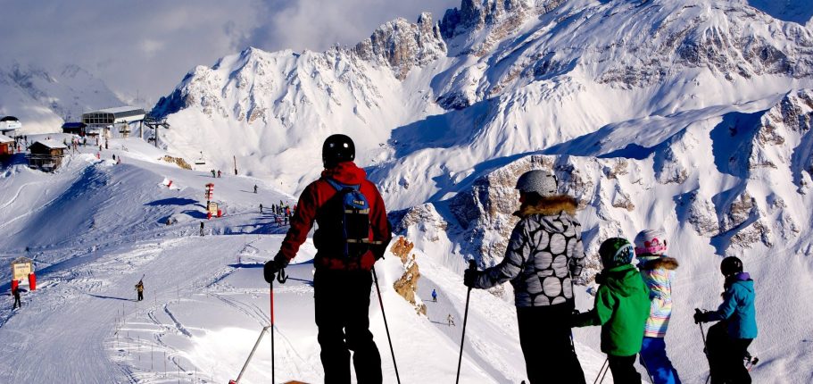 Skridskåkare på en snöig backe med fjäll i bakgrunden.