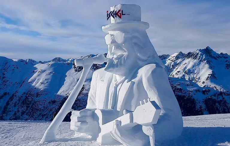 Snöskulptur av en man med hatt och skidor i fjällmiljö.