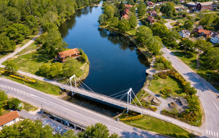 Vy över en bro som korsar en sjö, omgiven av grönska och bostäder.