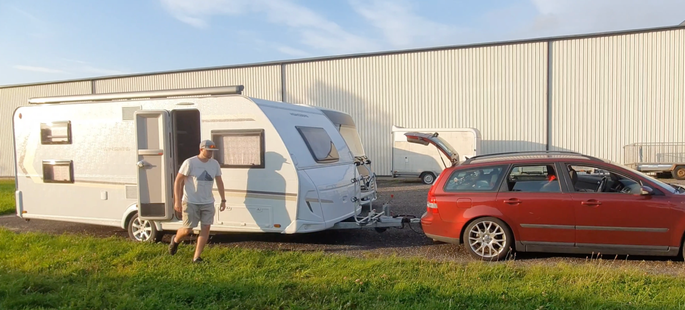 På väg En grå husvagn kopplad till en röd bil, med en person som går bredvid.