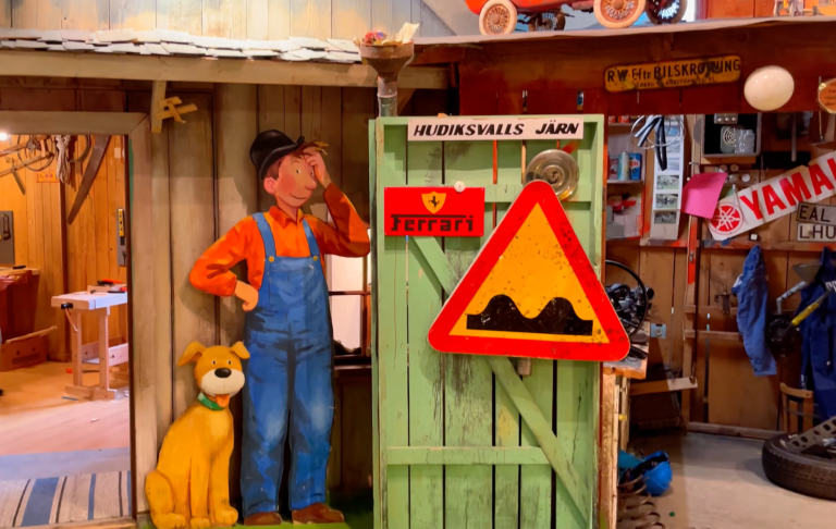 En figur av en pojke i overall står bredvid en hund och en varningsskylt inomhus.