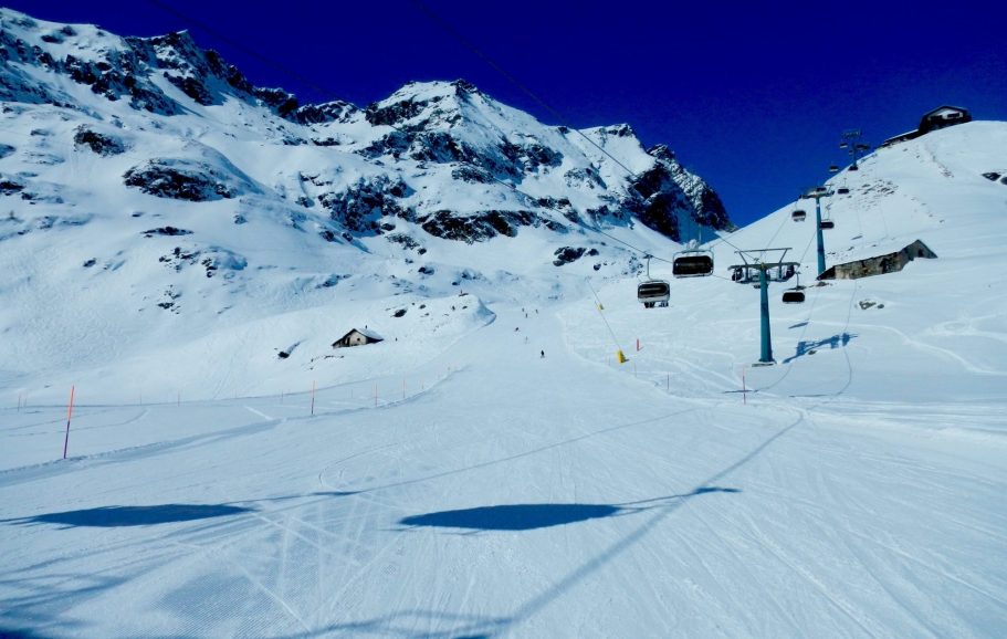 Snöigt alpinlandskap med berg och en skidbacke under klarblå himmel.