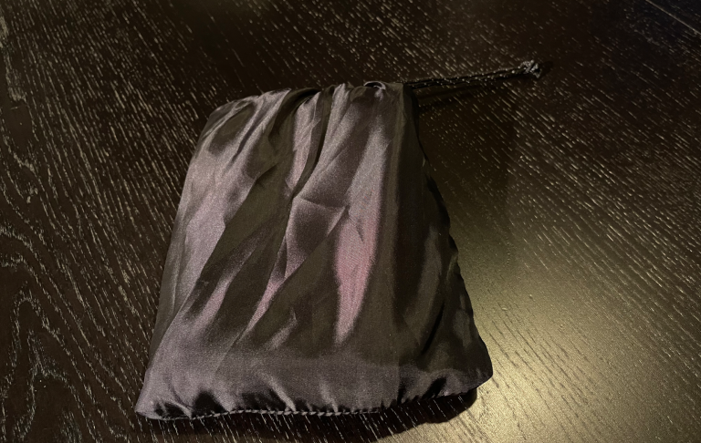 Svart klädespåse i satinmaterial, knuten i toppen.