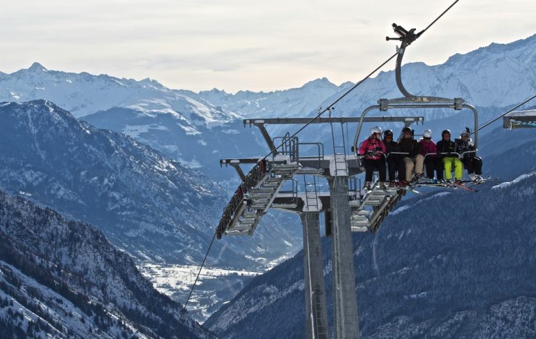 Sju personer åker skidlift över en snötäckt fjällandskap.