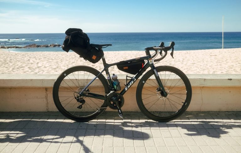 Cykel stående vid strandpromenad med havet i bakgrunden.