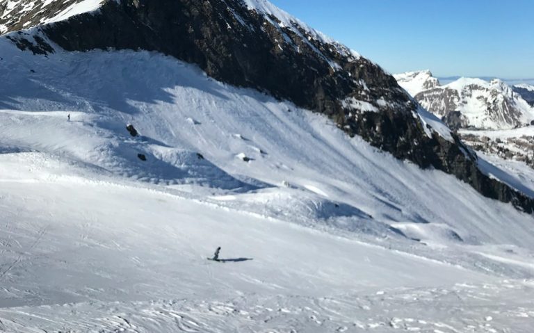 Snötäckt bergslandskap med en ensam skidåkare på en sluttning.