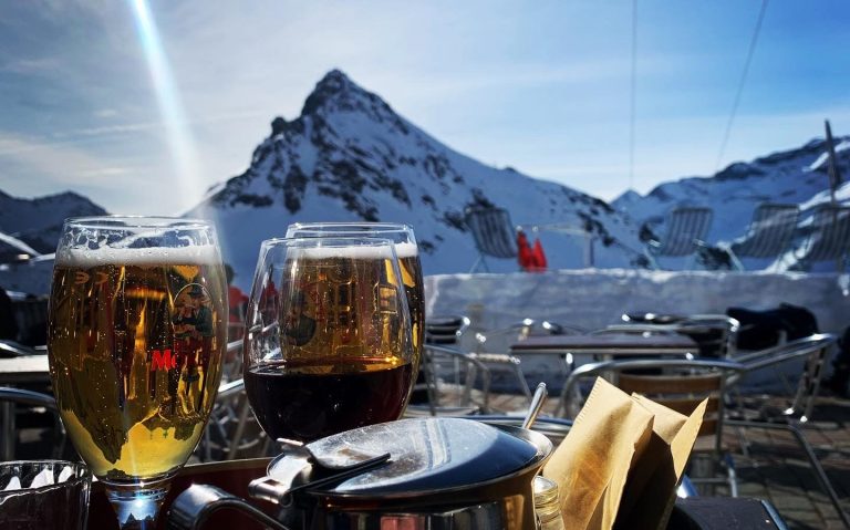 Två glas öl på ett bord med fjäll och klarblå himmel i bakgrunden.
