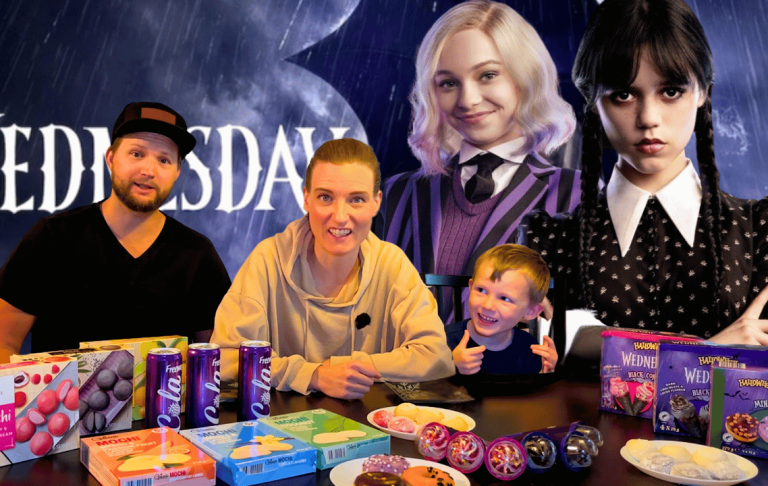 Tre personer poserar framför en stor väggbild, omgivna av snacks och godis.