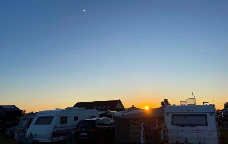 Solnedgång över camping med husvagnar och klara, blå himmel i bakgrunden.