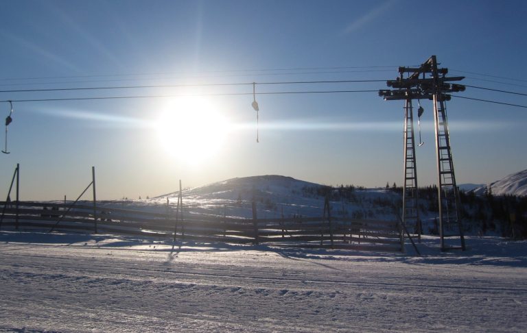 Sadeln och Tottliften i Soluppgång Vinterlandskap med snö, sol som skiner och liftstolpar i bakgrunden.
