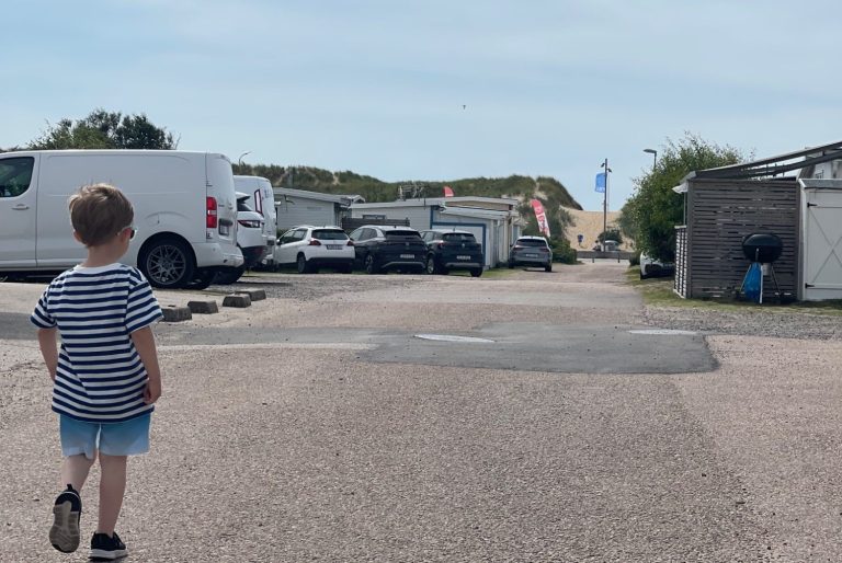 På Väg till Skrea Strand från Campingen En pojke går längs en asfaltväg mellan parkerade bilar och husvagnar.