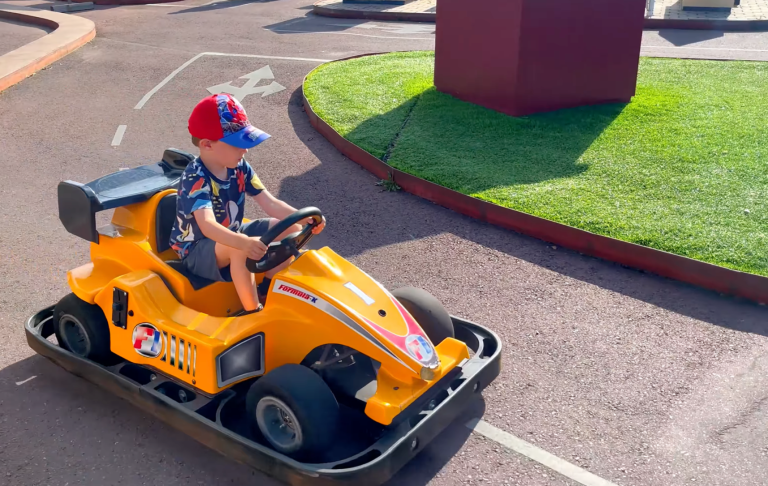 En liten pojke kör en gul go-kart på en bana.