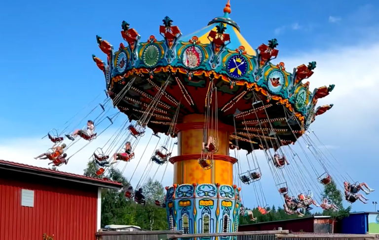 Snurrande karusell med färgglada säten och glada åkande i en nöjespark.