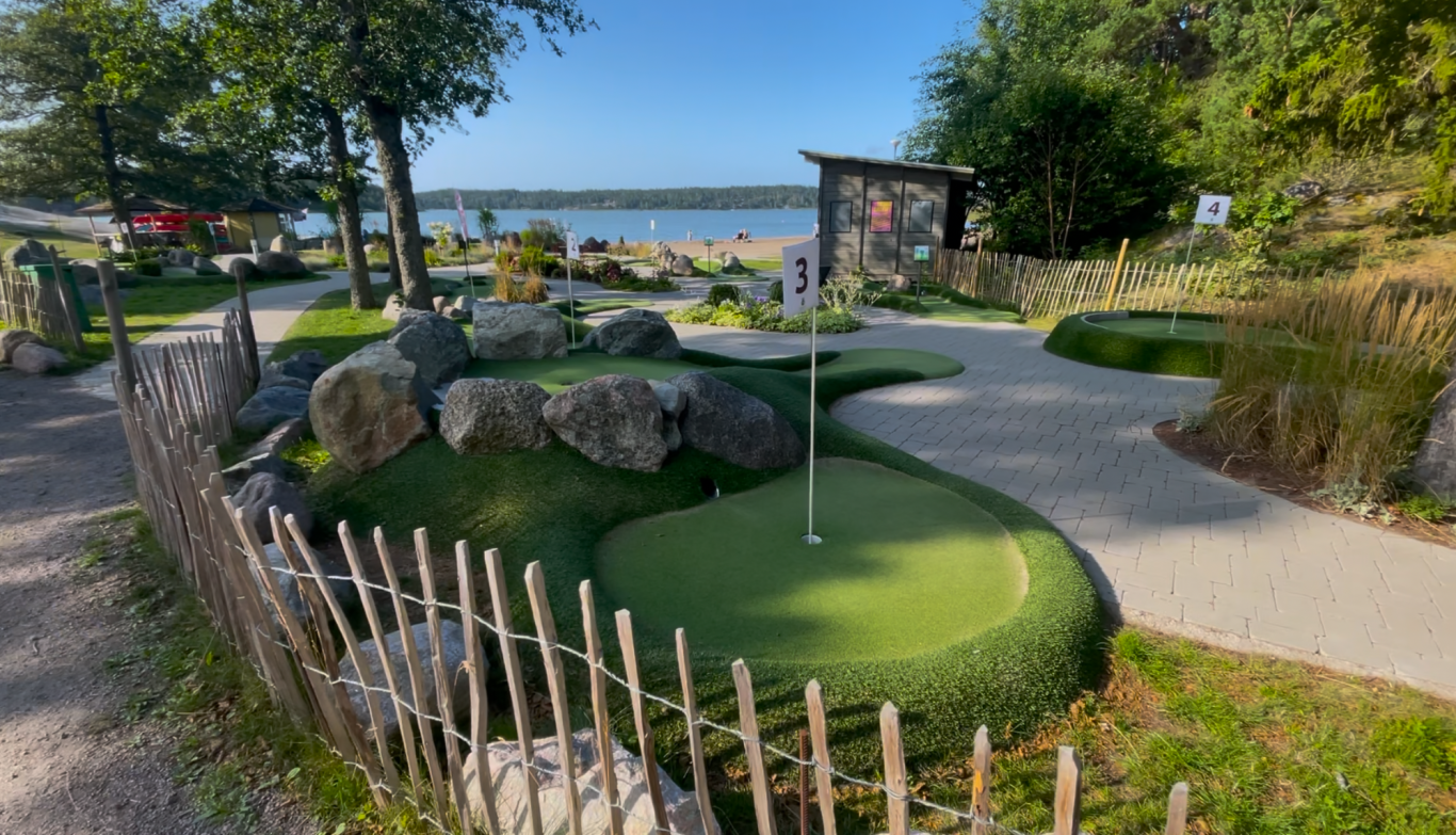 Minigolfbanan Minigolfbana med gröna fält, stenar och sjövy i bakgrunden.