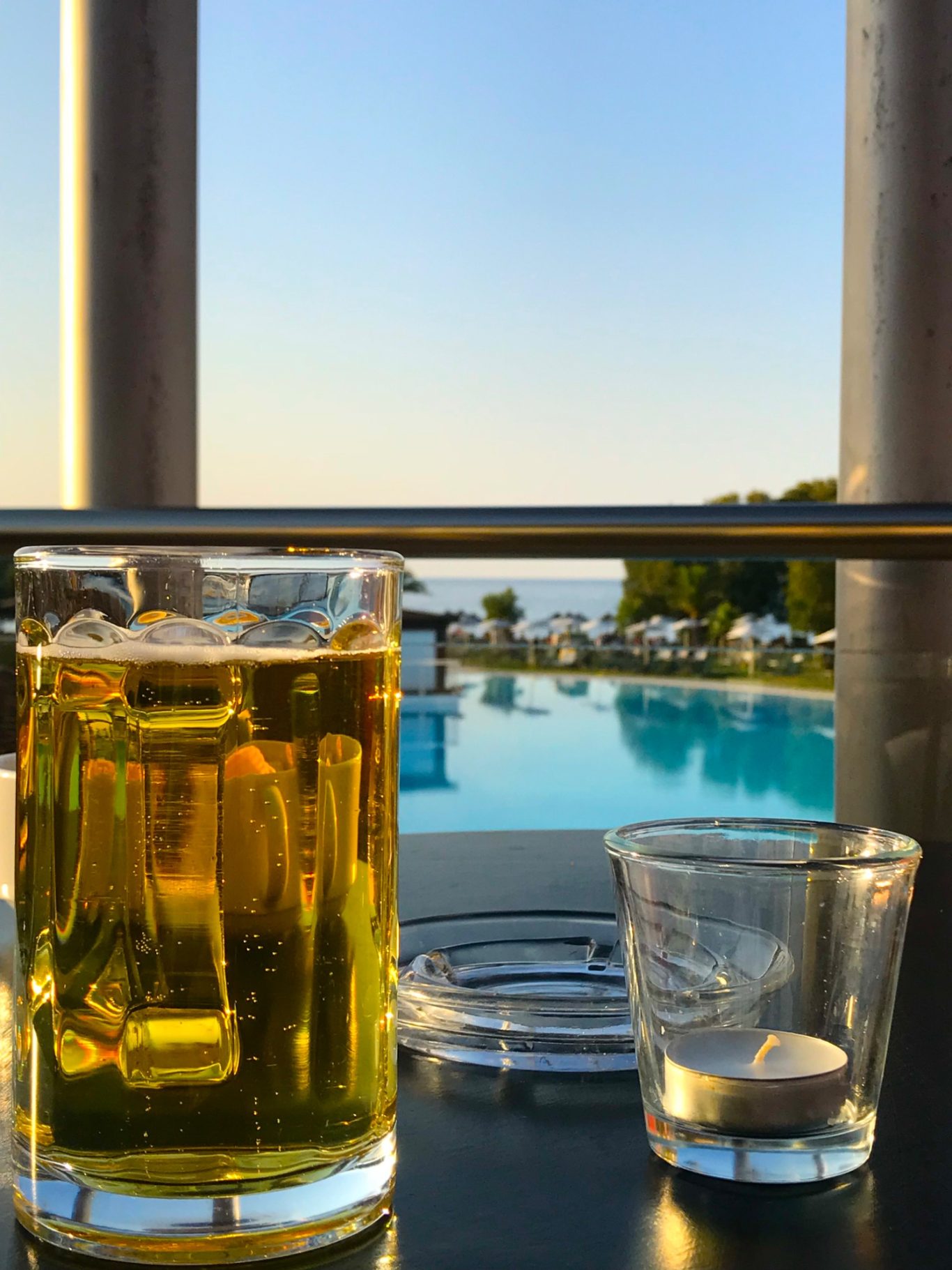 Öl Innan Middagen Ölglas och ett litet glas vid en pool med utsikt mot havet vid solnedgång.