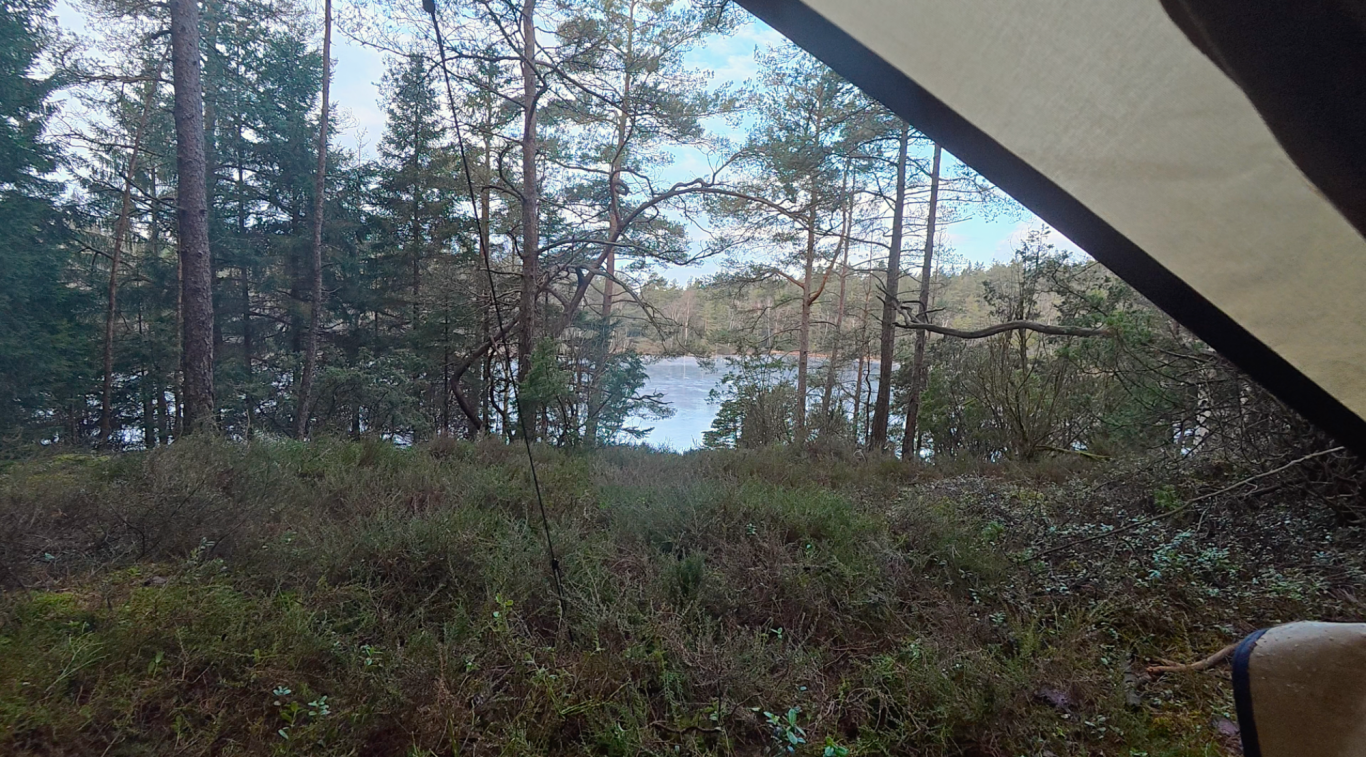 Utsikt över sjön Utsikt över en sjö omgiven av trädkantad terräng från ett tält.