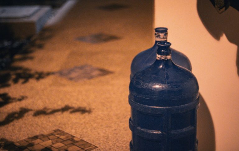 Blå vattenbehållare står på ett mönstrat golv i svagt ljus.