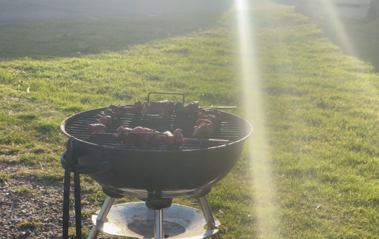 Grill med kött som tillagas på en solig gräsmatta.