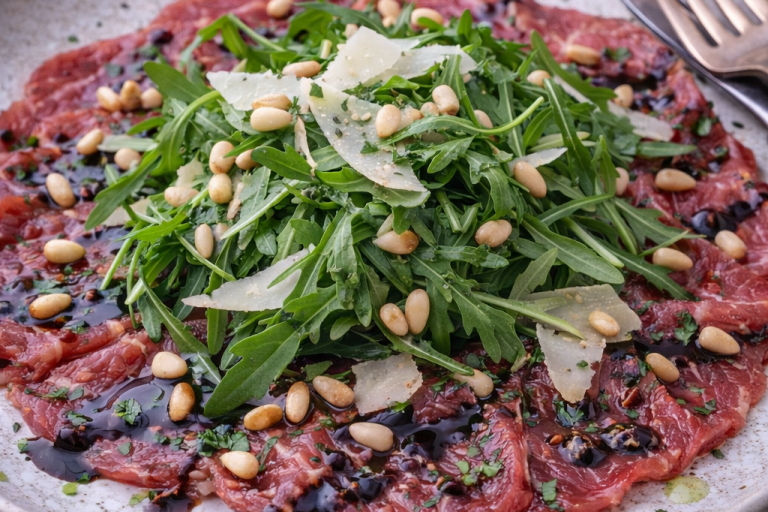Råbiff med ruccola, pinjenötter och parmesanost på en tallrik.