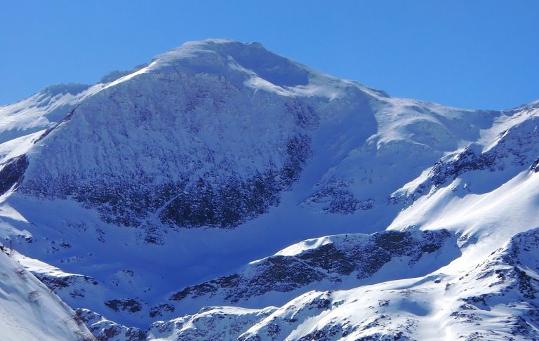 Skidbacke med stolslift och snöklädda fjäll i bakgrunden.