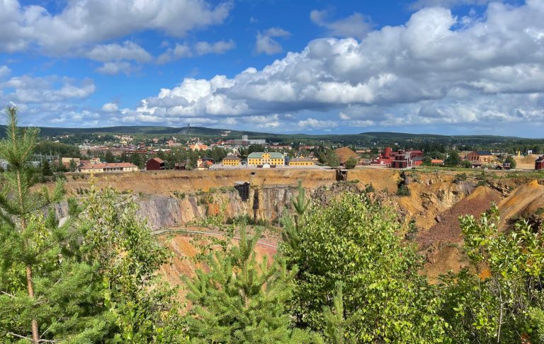 Utsikt över ett färgglatt landskap med berg och grönska under en blå himmel med moln.