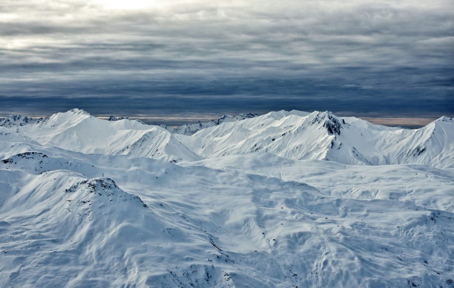 Snötäckta alpbergskedjor under en mörk himmel med grå moln.