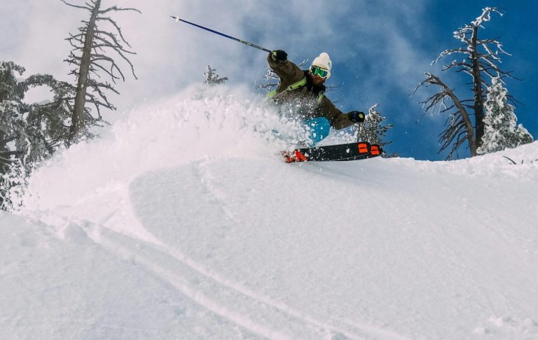 En snowboardåkare hoppar från en snötäckt sluttning under en klar blå himmel.