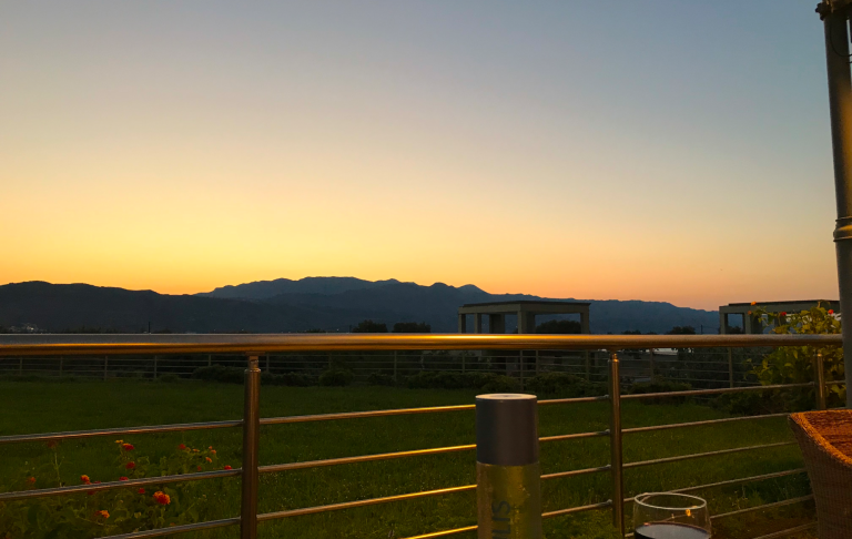 Solnedgång bakom berg med en railing i förgrunden.