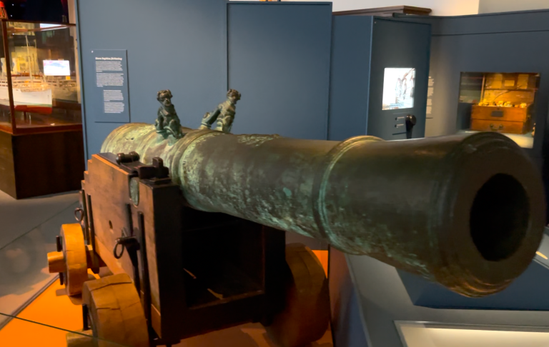 Historisk kanon i ett museum, med detaljerad yta och tre skulpturer på röret.