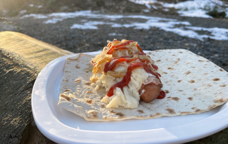 Tunnbrörulle med baconlindad ostkorv, mos och surkål med senap och ketchup. framför ett vinterlandskap.