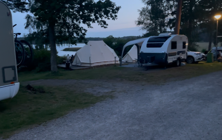 Campingområde med tält och husvagnar under skymning. Grönska i bakgrunden.