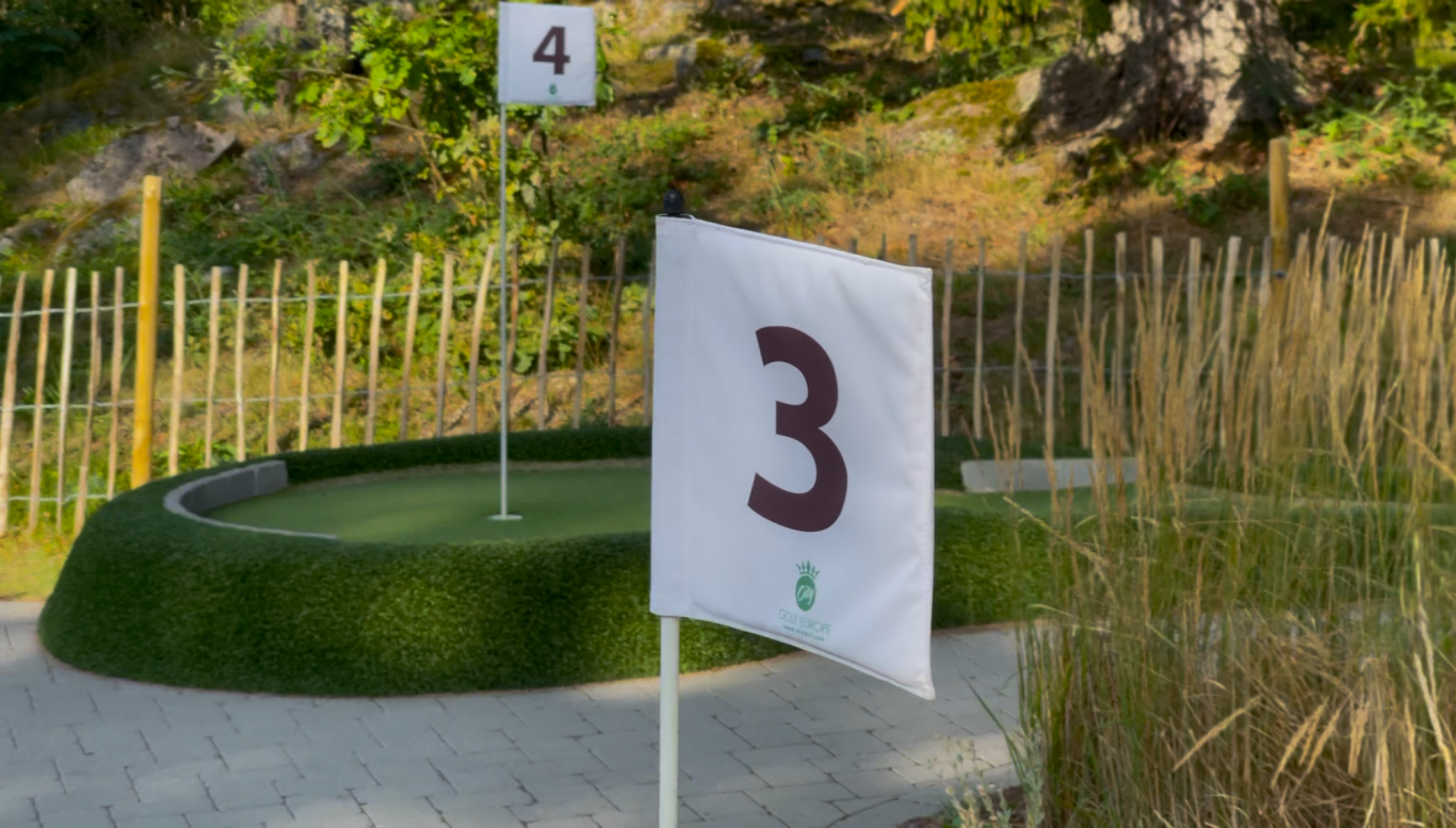 Minigolfen Flag with the number 3 in a miniature golf setting with greenery in the background.