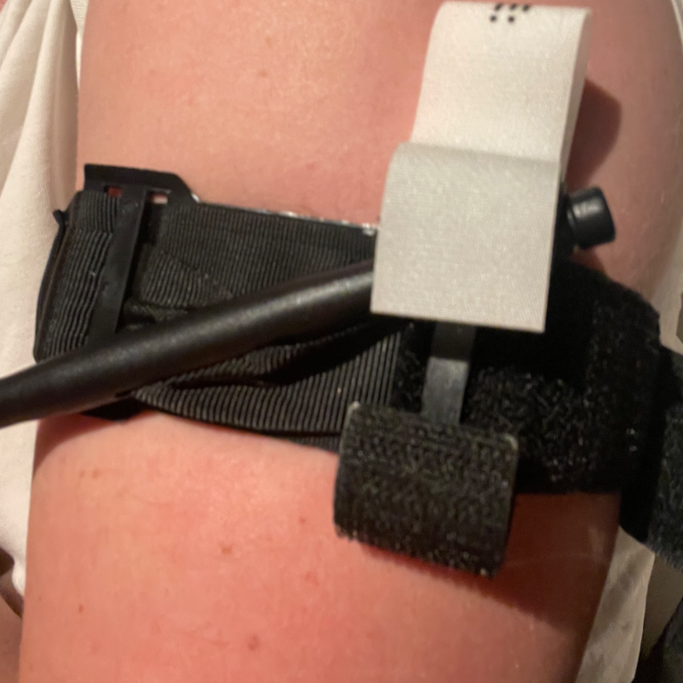 Svart bälte med remmar fäst vid en arm, en slang kopplad till en enhet.